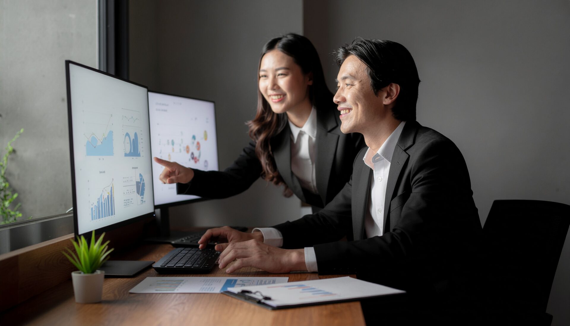 広報部門とマーケティング部門の担当者が、資料を持ち寄り、PC画面を見ながら連携している様子。SEOと広報の融合。