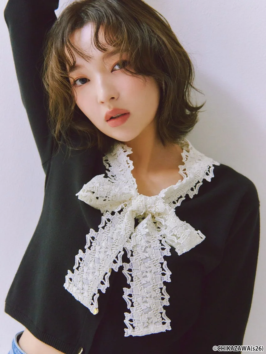 黒いトップスに白いレースのリボンをあしらった服を着てカメラを見つめる女性モデル