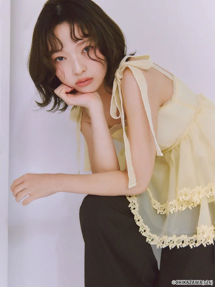 淡い黄色のレース付きトップスと黒いパンツを着用したショートヘアの女性モデル