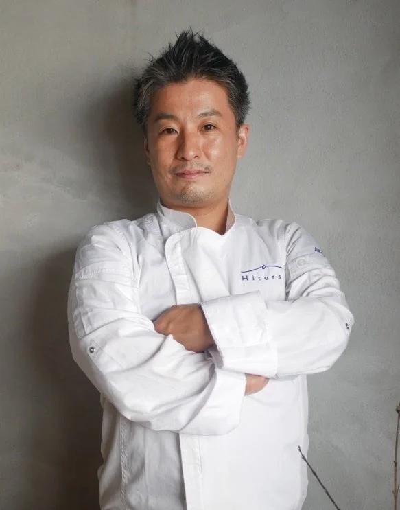 白いコックコートを着た男性が腕を組んで立っているポートレート写真