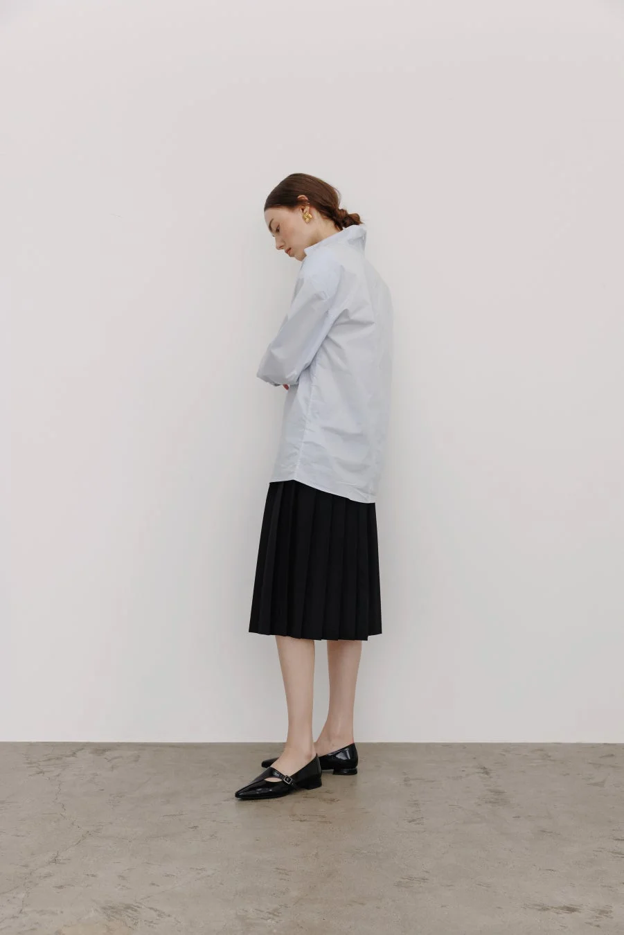 水色のシャツと黒いプリーツスカートを着用した女性の全身像