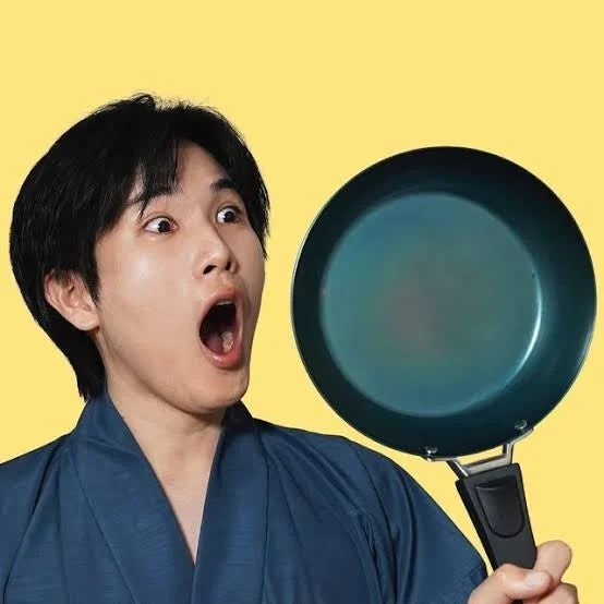 青い和服のような衣装を着た男性が、口を大きく開けて驚いた表情でフライパンを持っています。