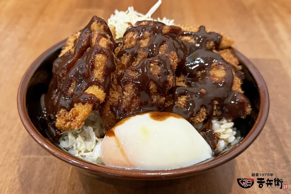 創業1979年の「吉兵衛」の神戸名物カツ丼。ご飯の上にサクサクの揚げカツが何枚も乗せられ、濃厚なソースがたっぷりかかっています。さらに、とろりとした温泉卵と千切りキャベツが添えられた、ボリューム満点の一品です。