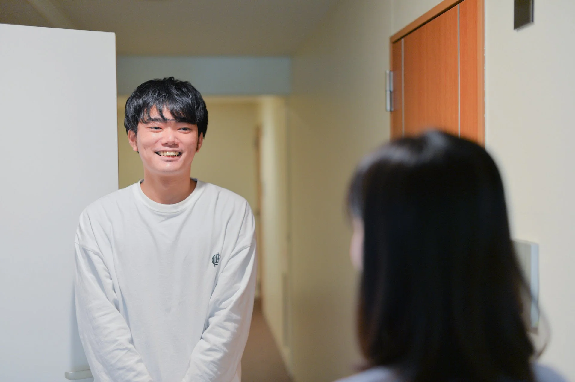笑顔の若い男性(しゅー先生)が屋内で誰かと向かい合っている様子