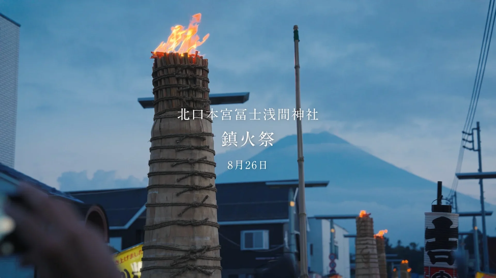 北口本宮富士浅間神社で開催される鎮火祭の様子。大きな篝火が燃え上がり、背景には富士山が見える。祭りの日程は8月26日を示す。