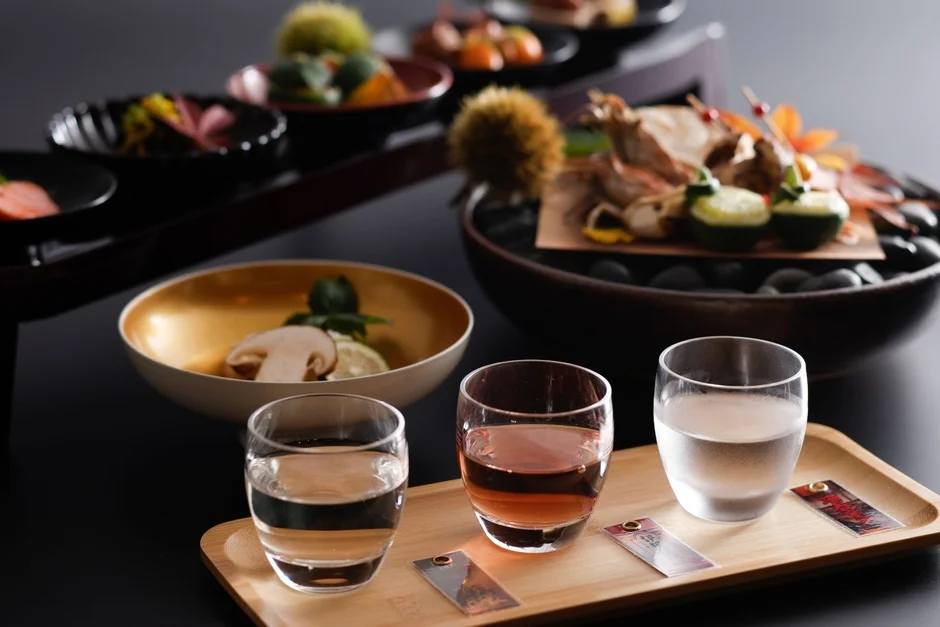 豪華な和食の懐石料理が美しく盛り付けられています。手前には3種類の飲み物が並び、奥には旬の食材を使った色とりどりの料理が並べられ、日本の繊細な食文化を感じさせます。