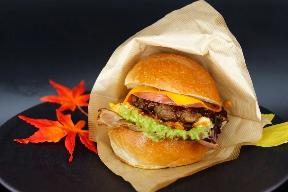 紙に包まれた具だくさんのハンバーガーと紅葉の葉
