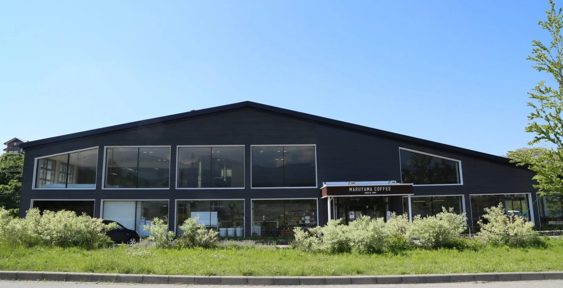 青い空の下、モダンな黒い外観の「MARUYAMA COFFEE」の店舗