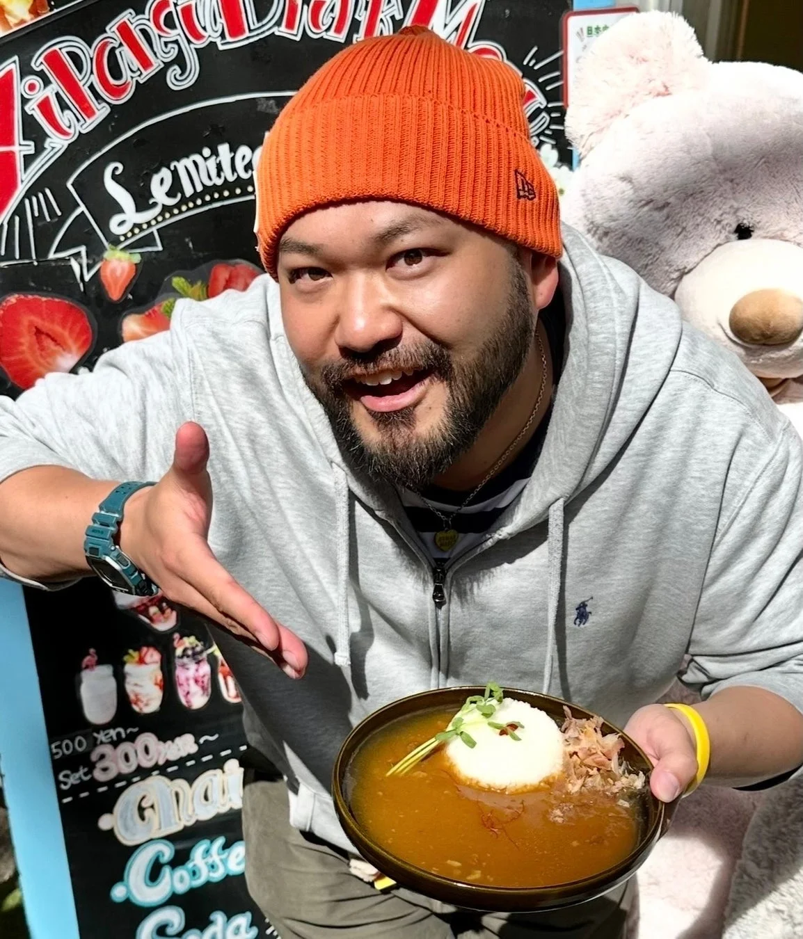 オレンジ色のニット帽をかぶった笑顔の男性が、美味しそうなカレーライスを手に持っている。