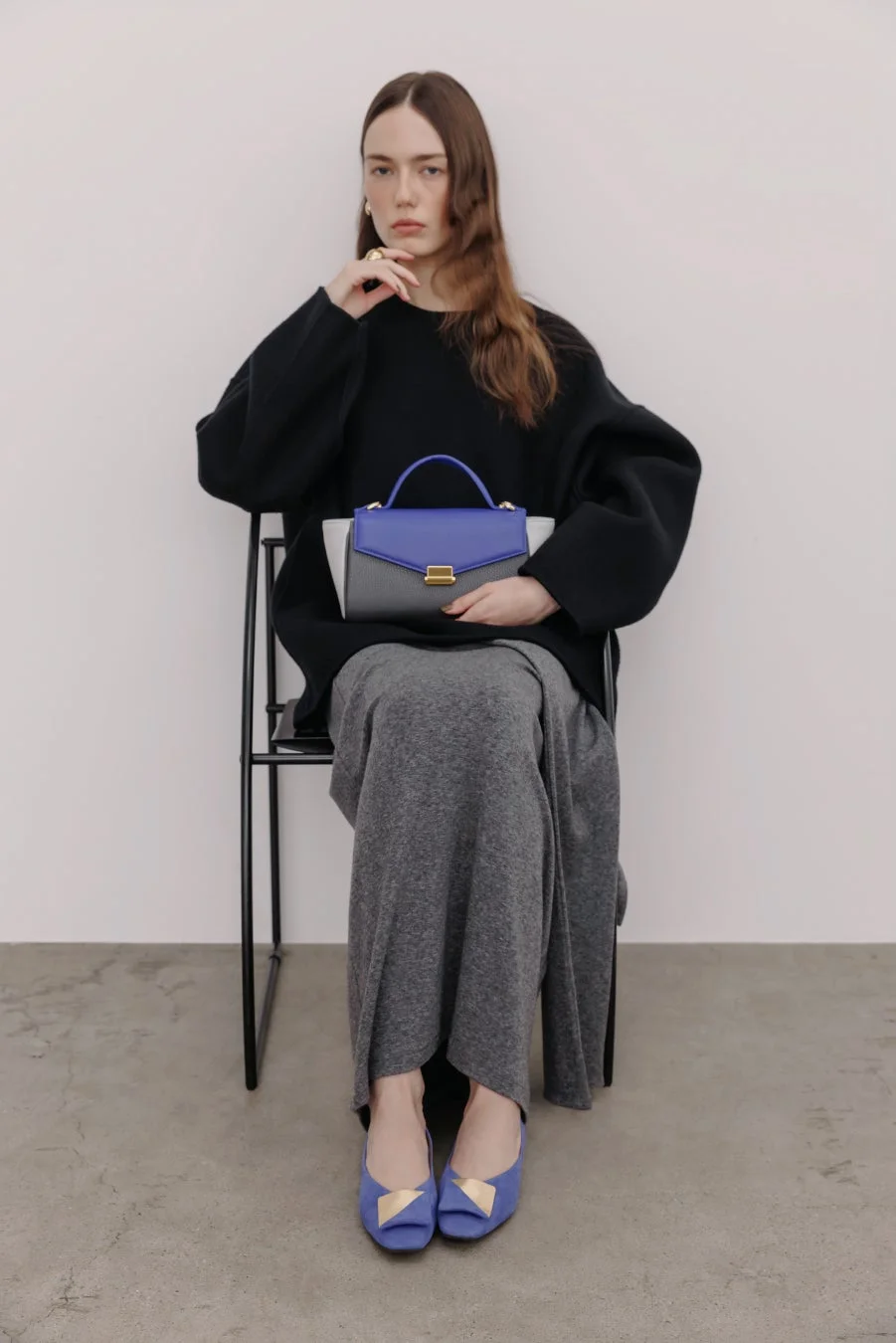 黒いセーターとグレーのスカートを着用した女性が青とグレーのハンドバッグ