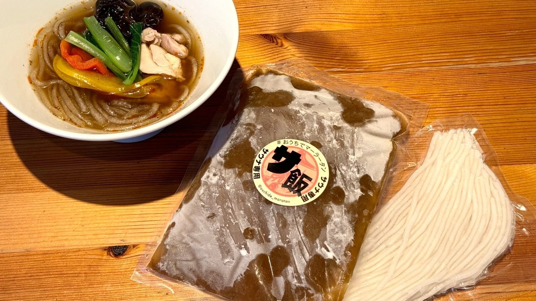 器に入った具だくさんのマーラータンと、調理前の冷凍スープと麺のパックが写っています。おうちで楽しめるサウナ飯をテーマにした冷凍食品であることがわかります。
