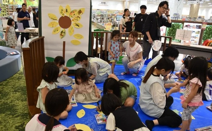 多くの親子が屋内でアート活動を楽しむ様子。壁にはひまわりの飾りが施されている。