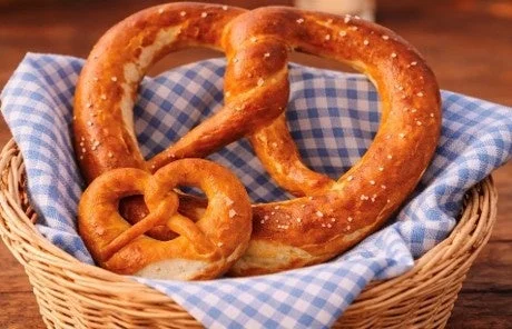 籐のバスケットに、青と白のチェック柄の布が敷かれ、大小2つの焼きたてのプレッツェルが置かれています。