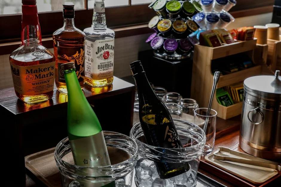 ホテルやラウンジのドリンクバー。ウイスキーや日本酒が氷で冷やされ、コーヒーポッドや茶葉も並んでいます。豊富な種類のアルコール飲料やソフトドリンクが楽しめるセルフサービスコーナーの様子です。