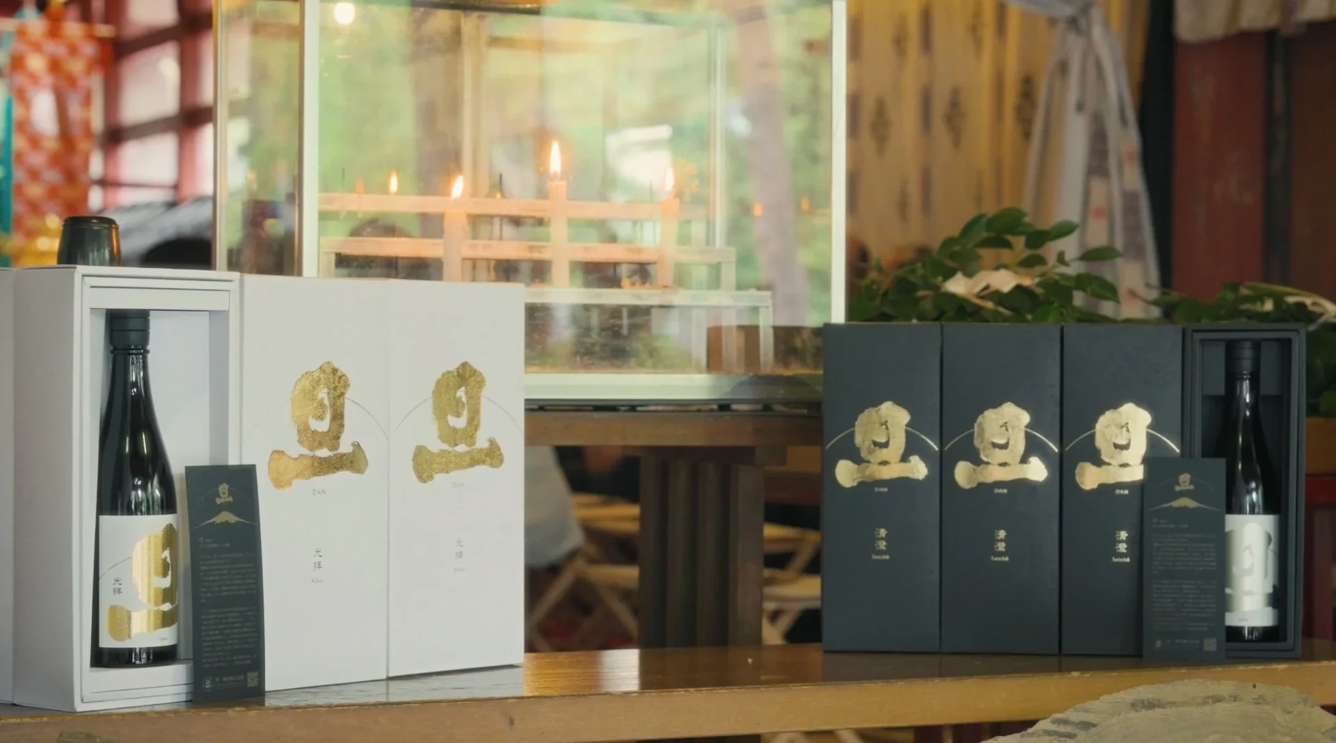 日本酒と思われる黒いボトルが、白と黒の高級感あるギフトボックスに収められ展示されています。背景にはろうそくが灯る飾り棚があり、和風で厳かな雰囲気が漂っています。