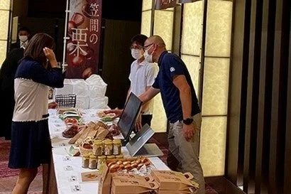 屋内イベント会場の販売ブースで、客と店員が商品について話している様子