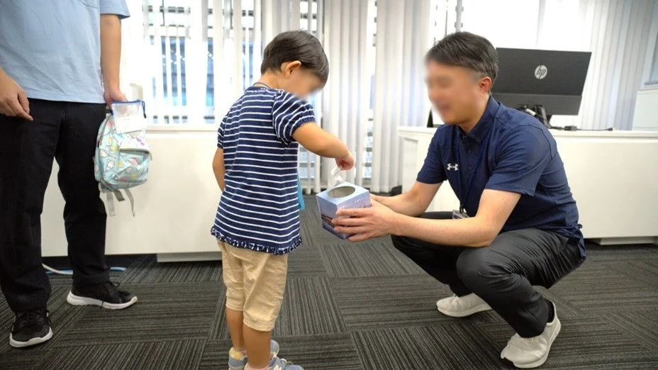 子供がかがんだ男性と箱を使って交流している様子です。