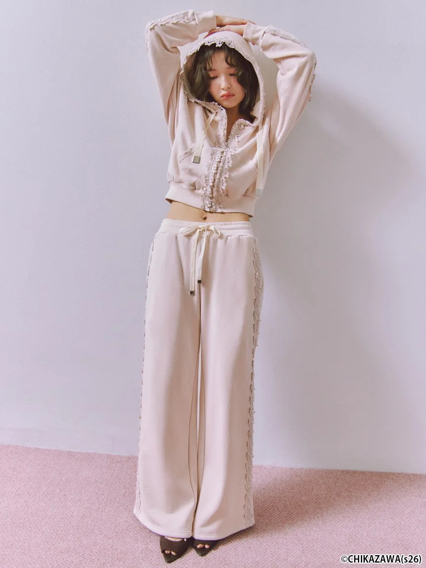 淡いピンクベージュのレースがあしらわれたクロップド丈パーカーとワイドパンツのセットアップを着用した女性モデル