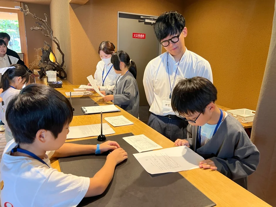 子供たちが大人と一緒にカウンターで書類に目を通したり、手続きを行ったりしている様子