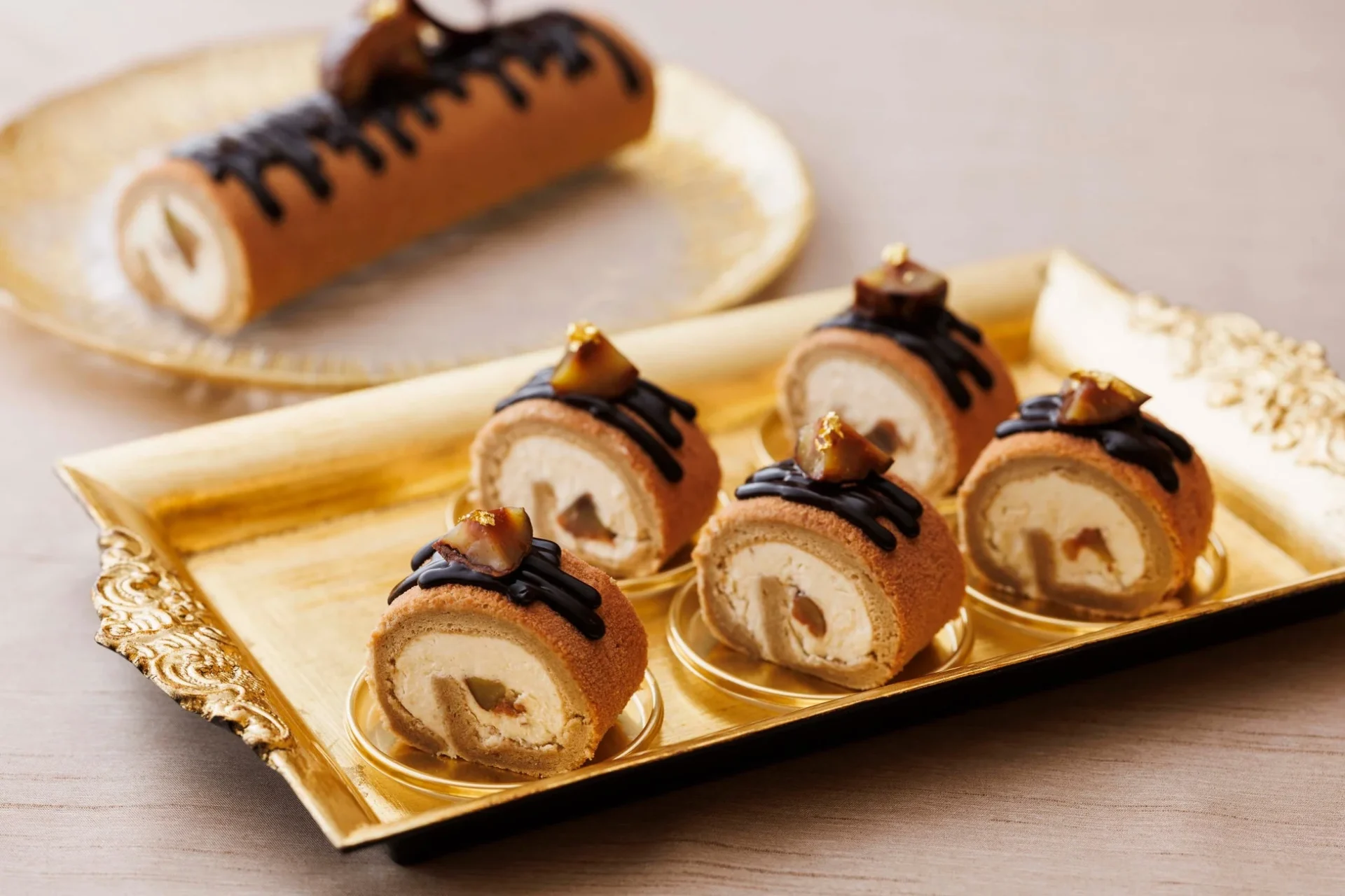 豪華な金色のトレーに盛り付けられた、栗とチョコレートで飾られたロールケーキのセット