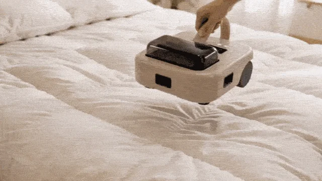 白い布団の上を掃除するAIクリーナーロボ