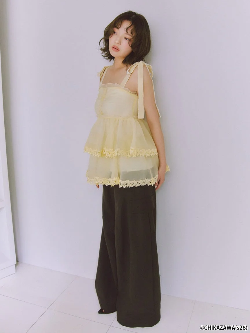 肩リボンの付いた淡いイエローのティアードトップスとダークカラーのワイドパンツを着用した女性モデル