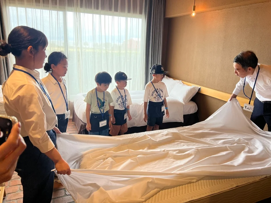 ホテルの一室で、子供たちがスタッフからベッドメイキングの指導を受けている