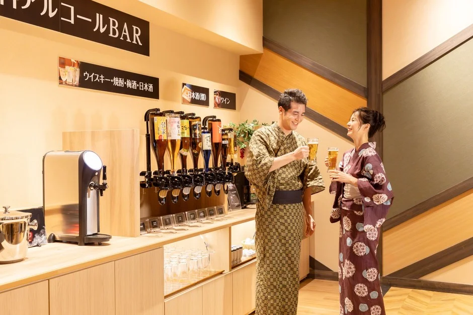 浴衣姿の男女がアルコールバーでビールを片手に笑顔で乾杯している瞬間を捉えた画像です。