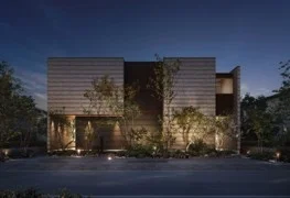 夜間にライトアップされたモダンなデザインの住宅。木々が植えられた庭が建物の外観を引き立て、洗練された雰囲気を醸し出している。