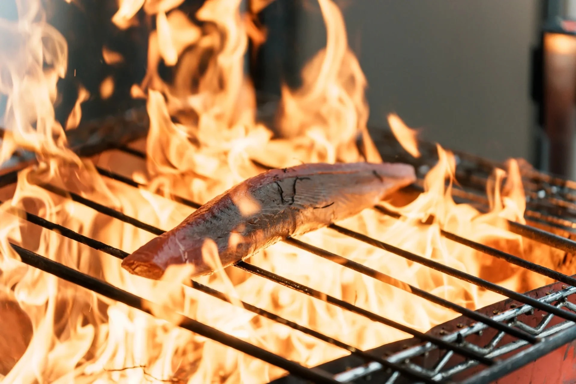 炎が勢いよく燃え上がるバーベキューグリルで魚を炙る様子