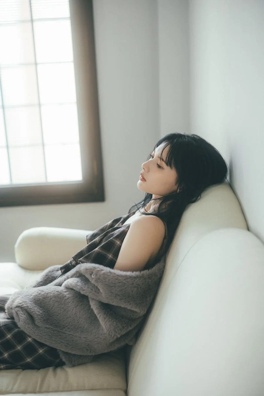 窓からの光が差し込む部屋で白いソファに寄りかかる女性