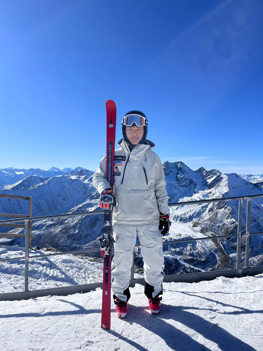 晴れた雪山でスキー板を抱えて立つスキーヤーの女性