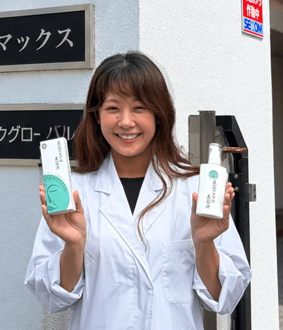 白衣の女性が笑顔で「美容マスクの美容液」の箱とボトルを持っている