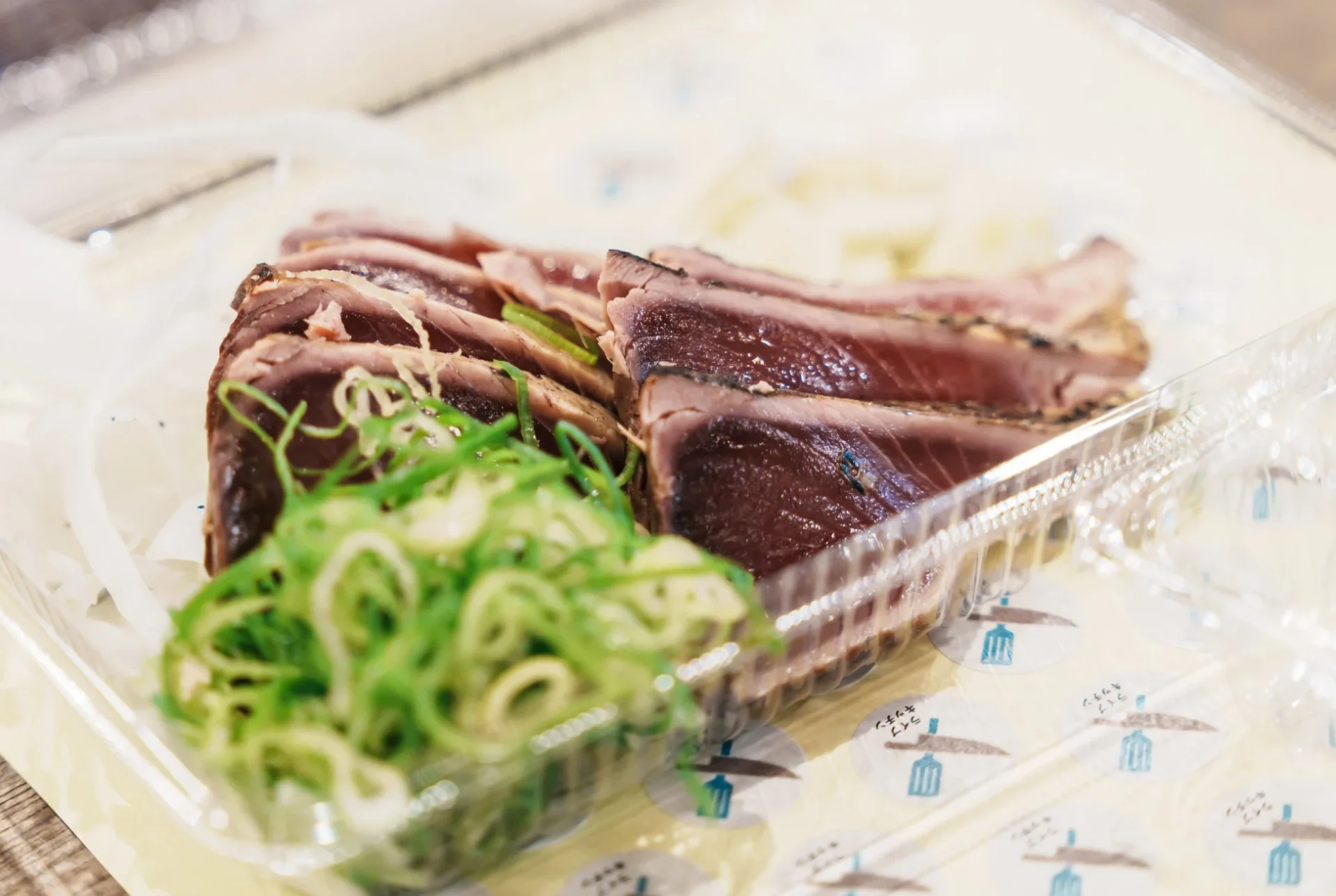 プラスチック容器に盛り付けられたカツオのたたきとネギ