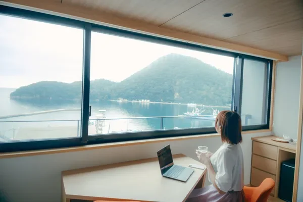窓から海の見える部屋でノートパソコンに向かう女性