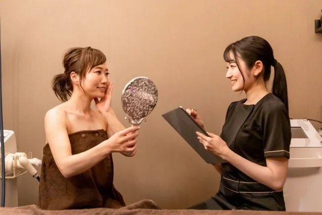 エステサロンで鏡を見る女性とエステティシャン、カウンセリング