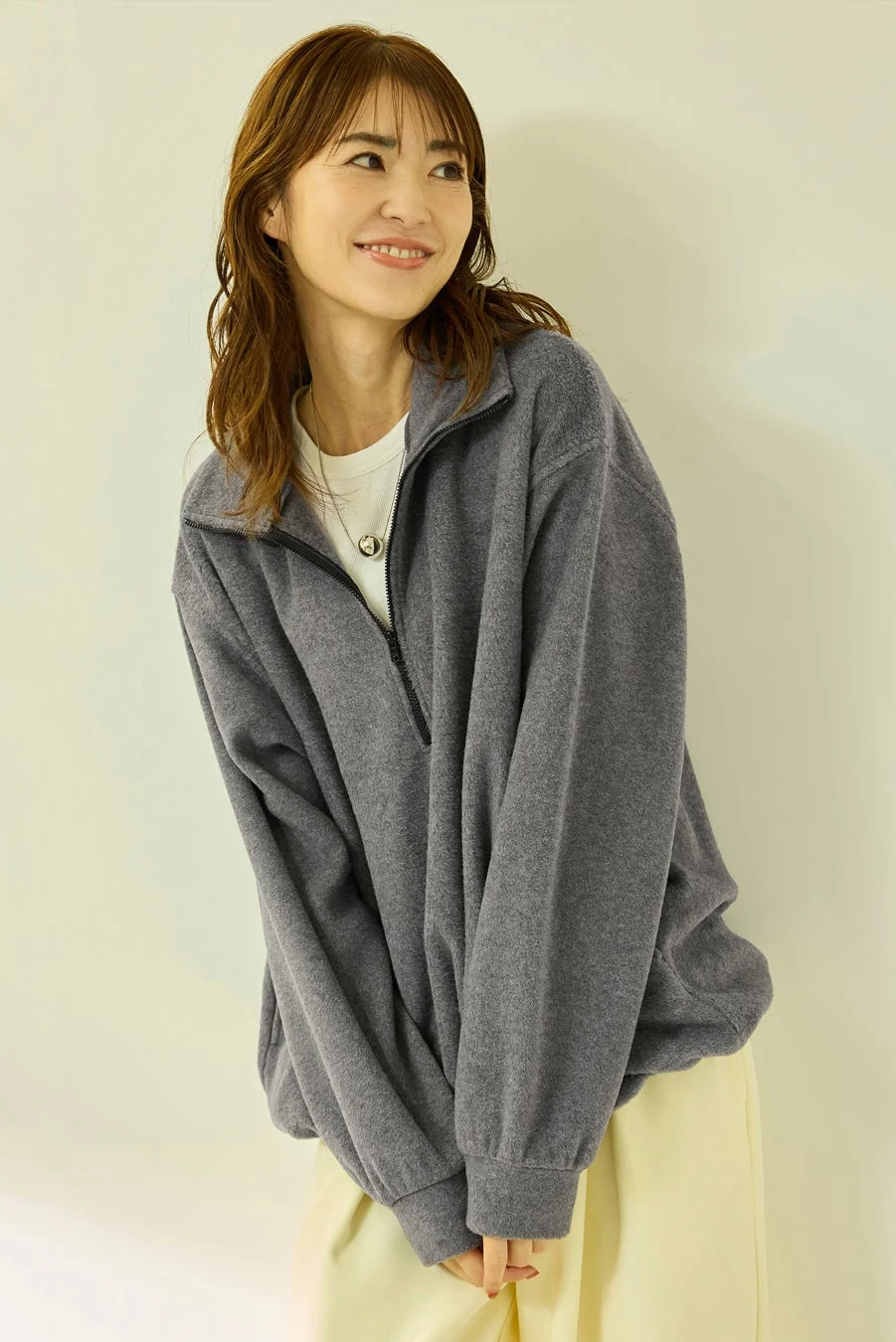 笑顔で横を向いている女性がグレーのオーバーサイズフリースを着用