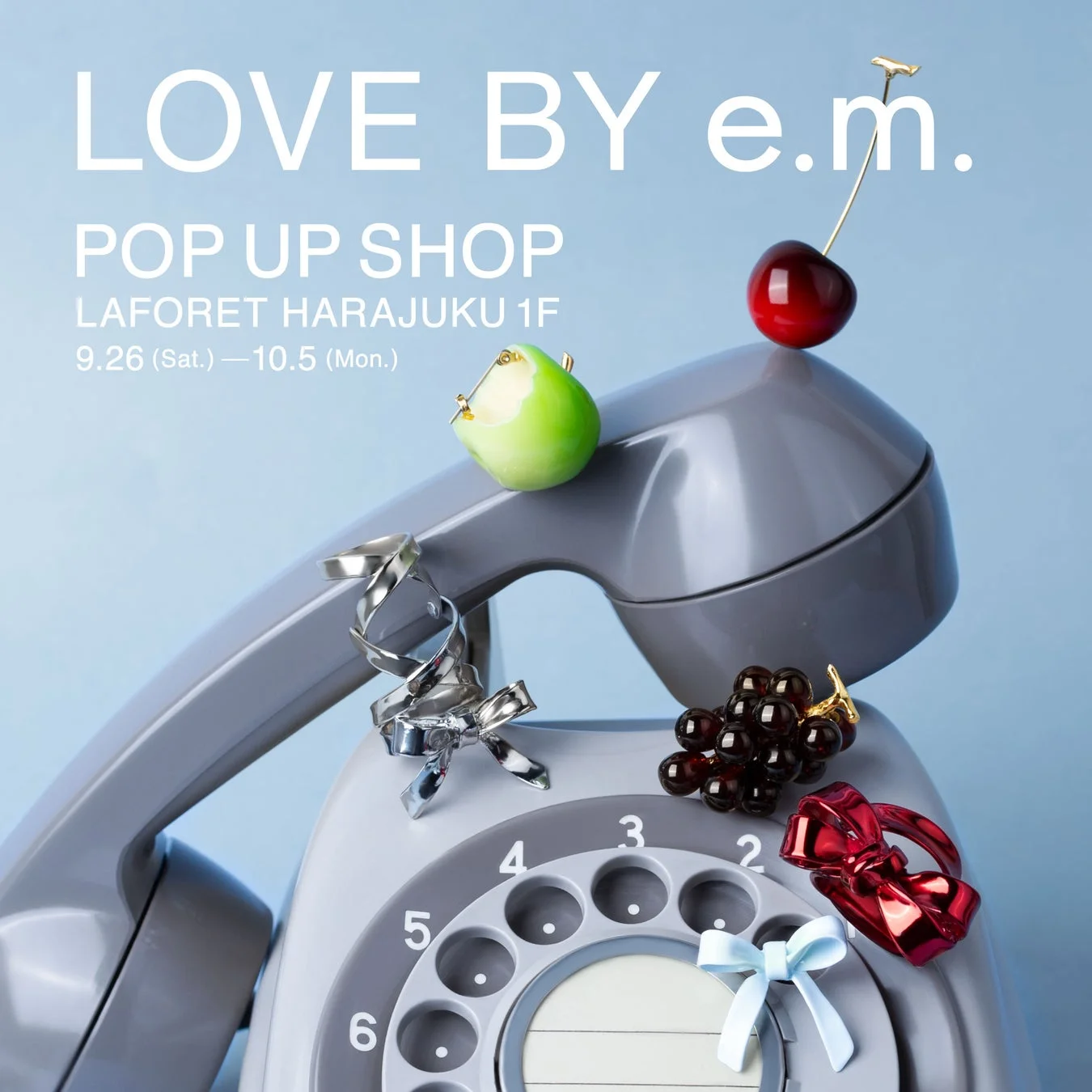 レトロなダイヤル式電話機の上に、フルーツやリボンを模したアクセサリーが飾られた、e.m.のポップアップショップ開催を告知する画像です。ラフォーレ原宿で9月26日から10月5日まで開催されます。