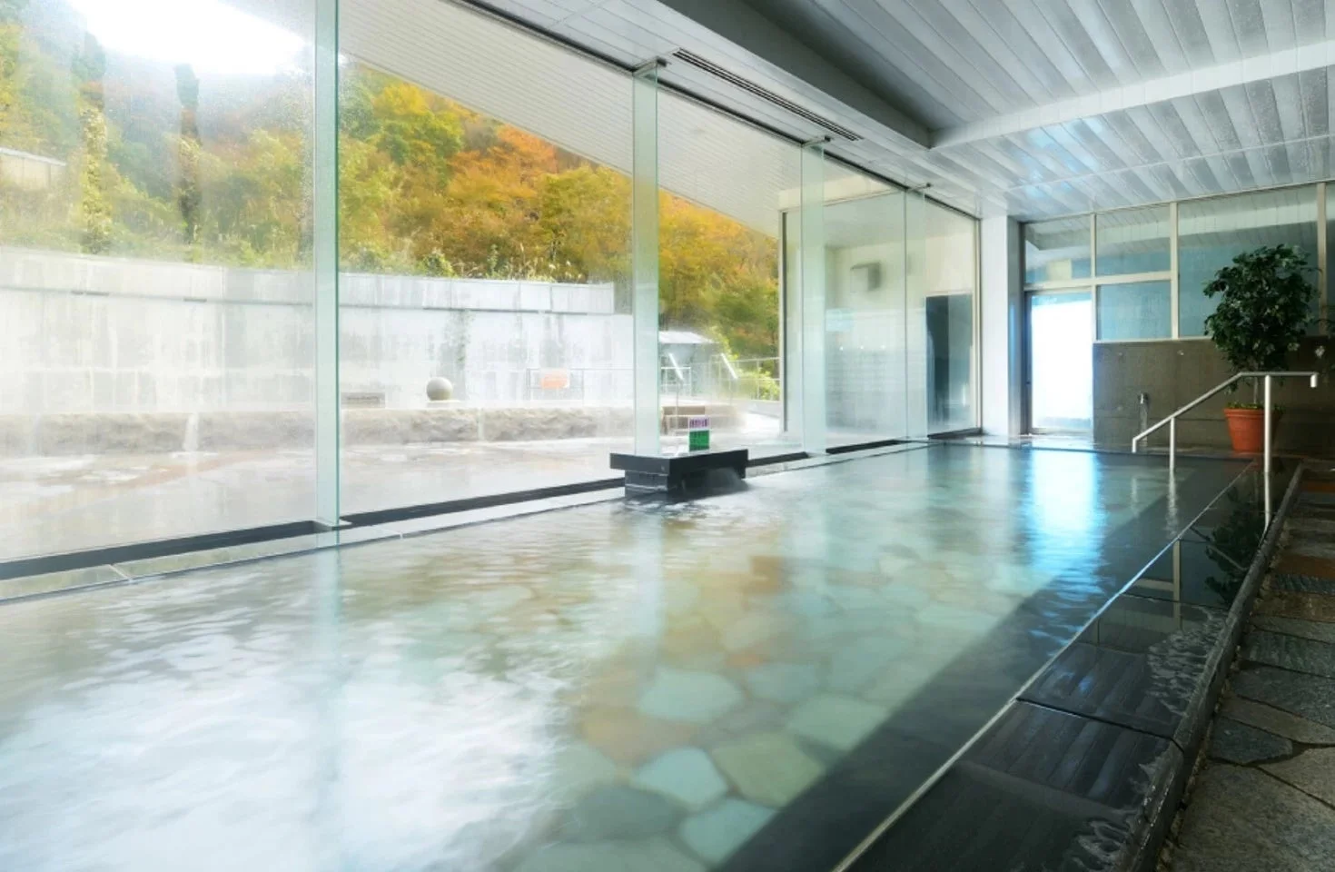 大きな窓から美しい紅葉が広がる秋の自然を望む、開放感のある屋内温泉施設