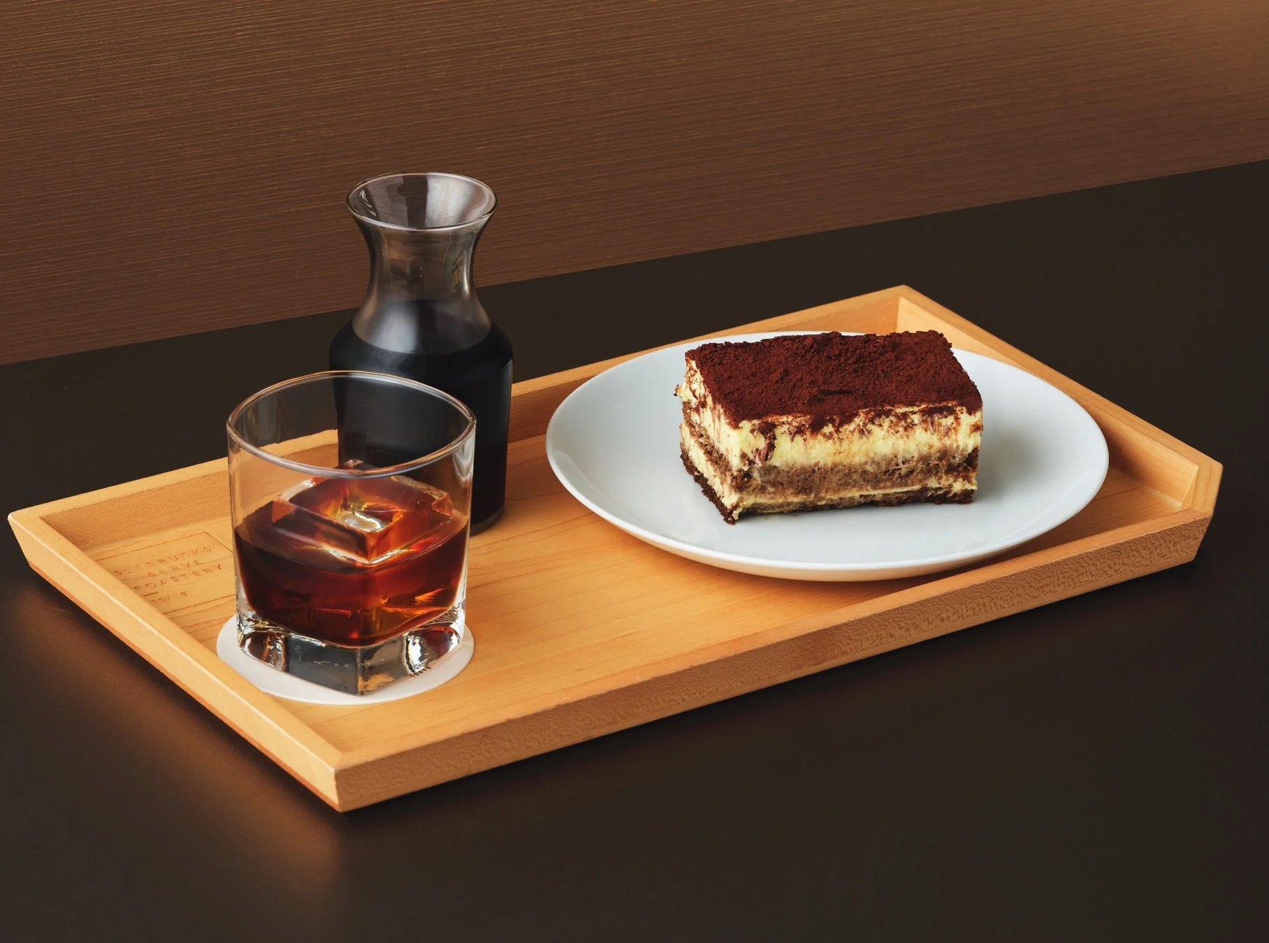 木のトレイにティラミスとアイスコーヒーが並べられた、カフェのデザートセット