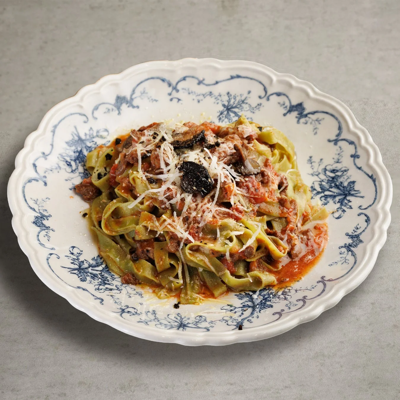 緑色のタリアテッレにボロネーゼソースとトリュフがトッピングされたパスタ