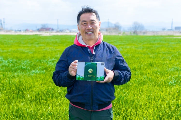 百明青汁の箱を持つ生産者の中野氏