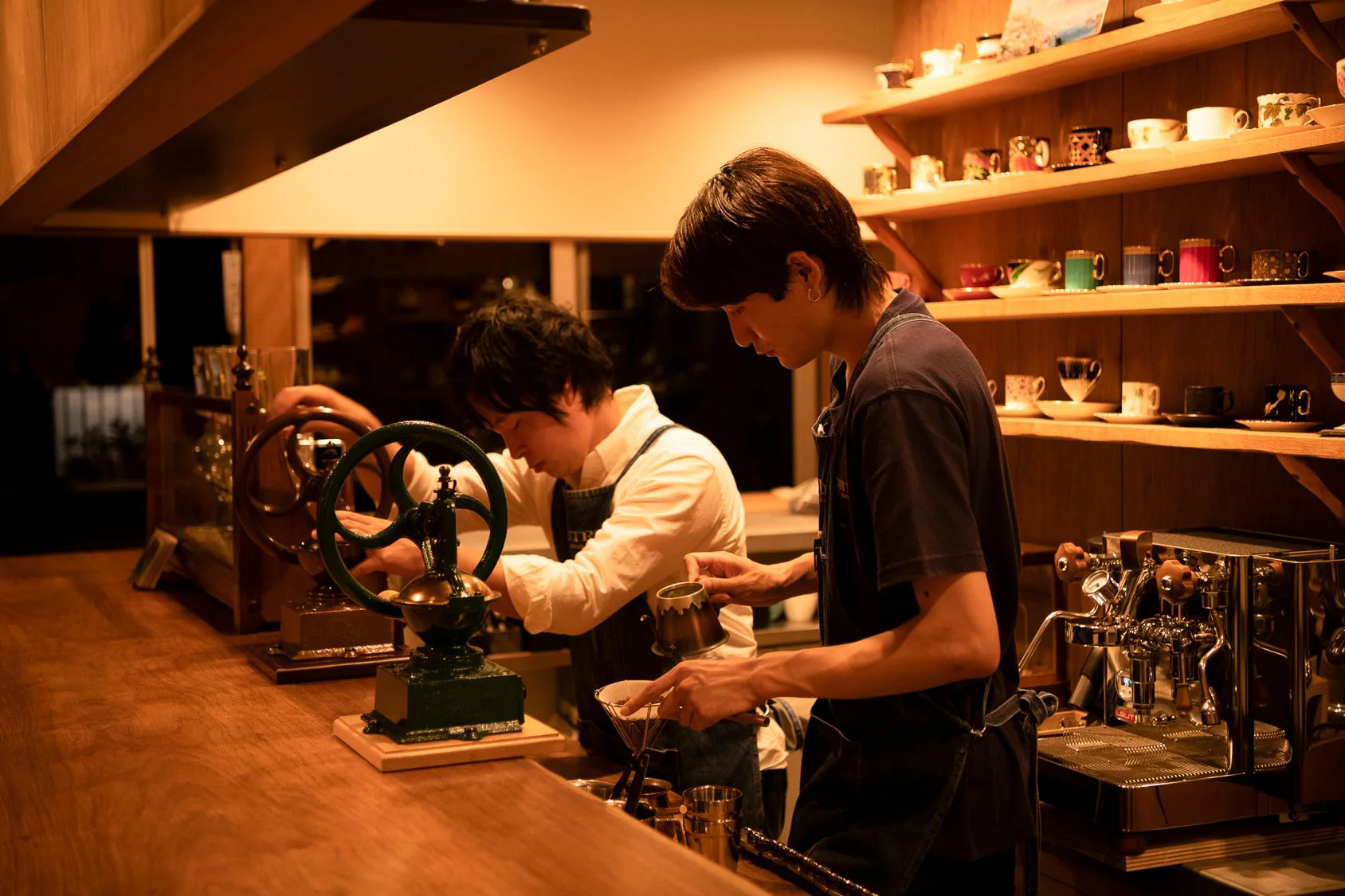温かい雰囲気のコーヒーショップで、二人のバリスタがコーヒーを淹れている様子