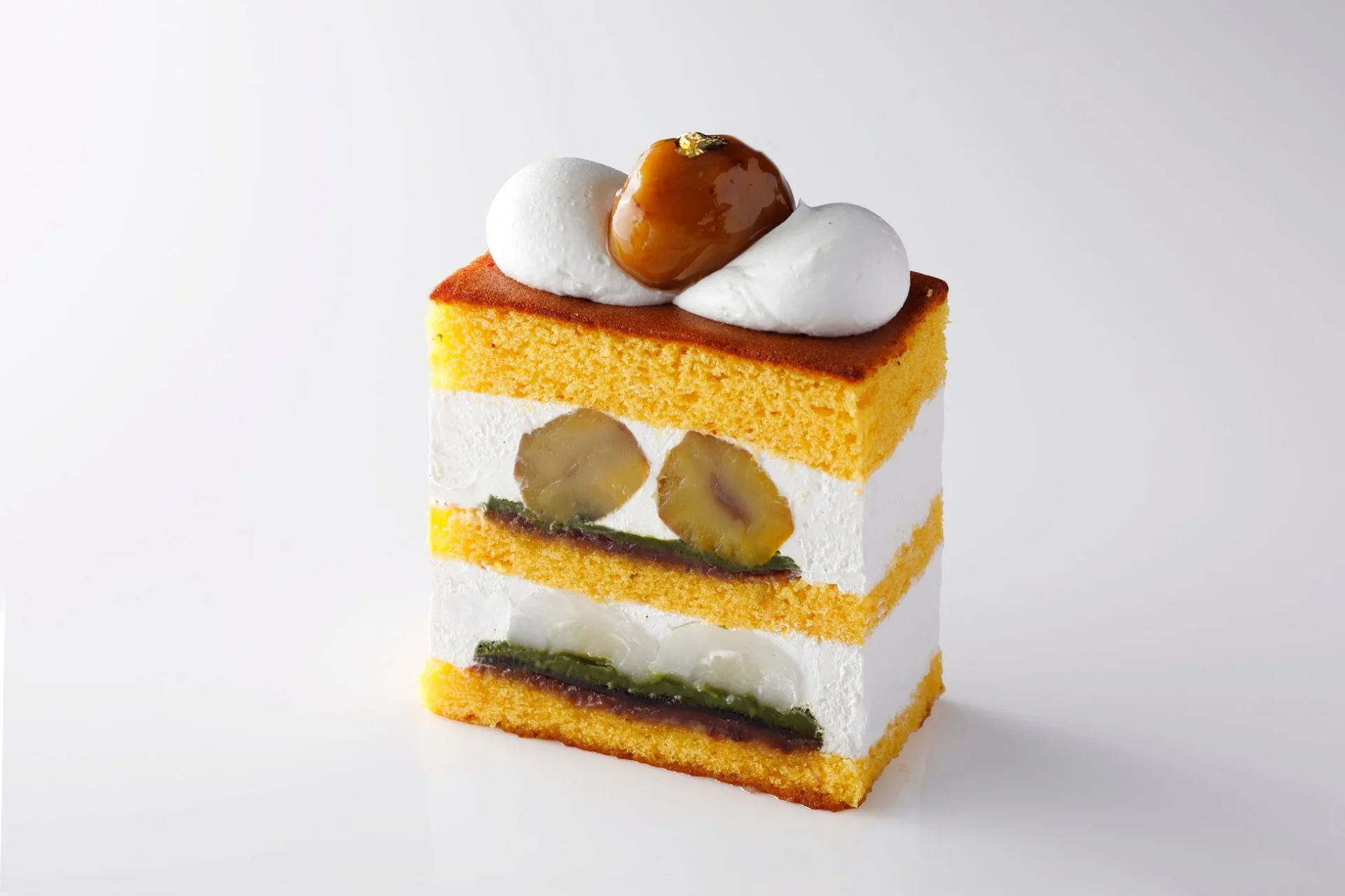 白い背景に、層になった和洋折衷の美しいモンブランケーキが写っています。スポンジケーキとクリームの間に栗、抹茶、あんこが挟まれ、上には艶やかな栗とホイップクリームが飾られています。