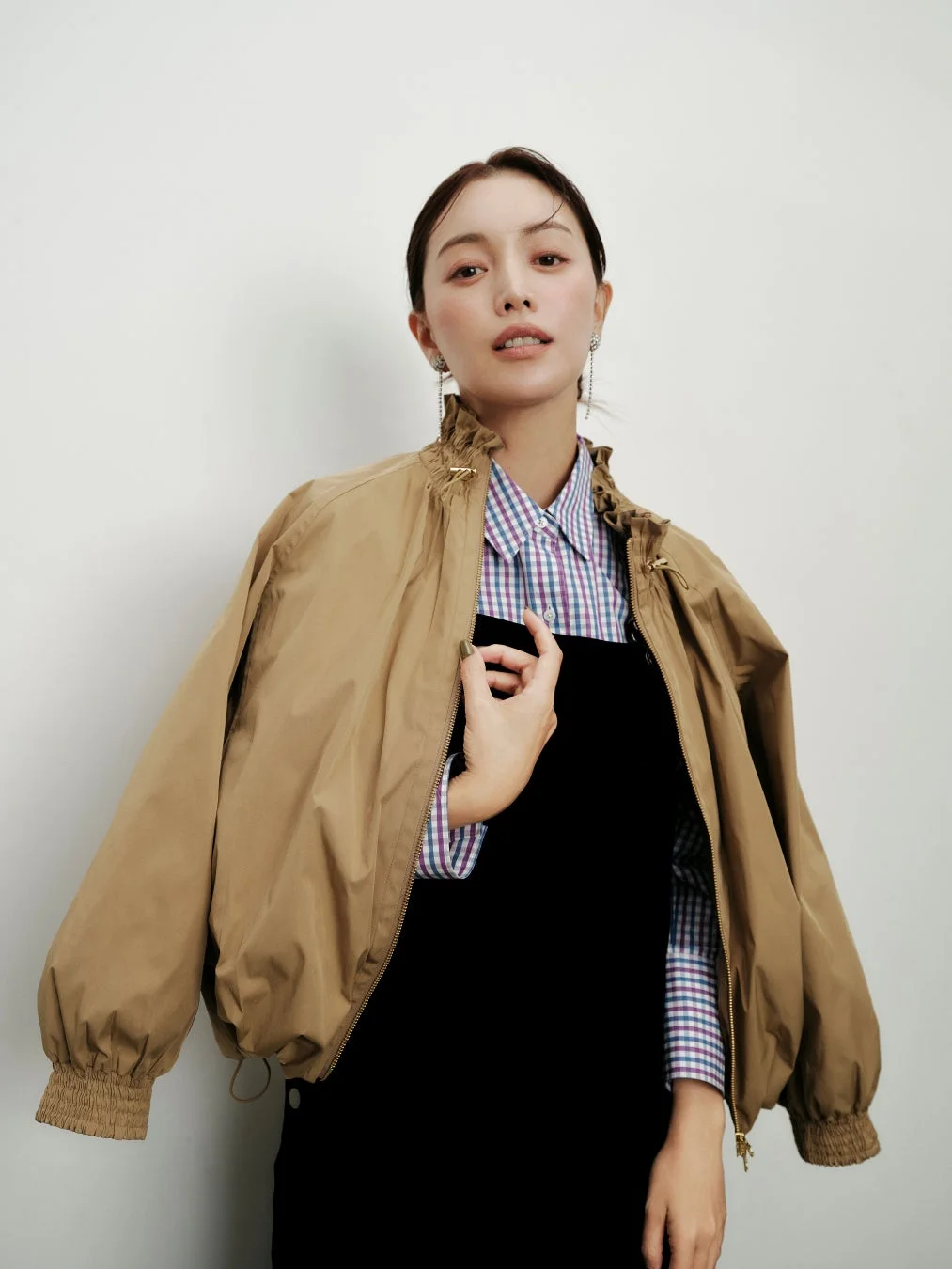 ベージュのボンバージャケットを肩にかけ、チェックシャツと黒いトップスを着用している女性のポートレート