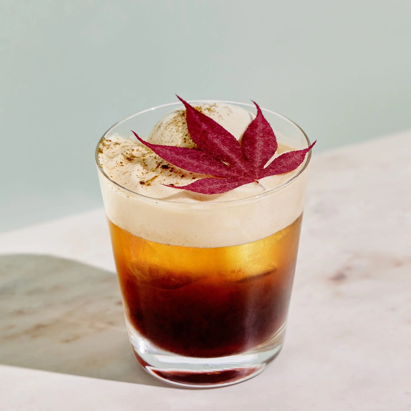 グラスに入った冷たい飲み物で、上には白いクリームとアイスクリーム、そして赤いモミジの葉が飾られています